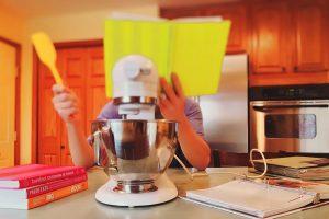 A person behind a yellow book in a kitchen, standing in front of some kitchen appliance.