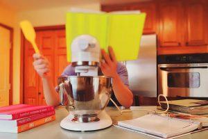 A person behind a yellow book in a kitchen, standing in front of some kitchen appliance. 