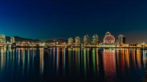 An image of Vancouver at nighttime. The picture is that of a city seen from some boat on a body of water. Moving to Canada means enjoying all the benefits this city has to offer. 