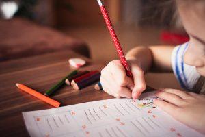 A child writing something with a red pen. Moving during the school year implies transporting all of your child`s school supplies.