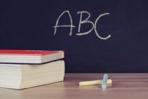 A blackboard with abc written on it. two books and some yellow and blue chalk.