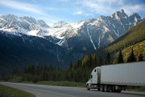 A moving truck on the road, in the middle of a natural setting. 