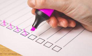 A close up of a person holding a pink marker and ticking off items on a checklist. 