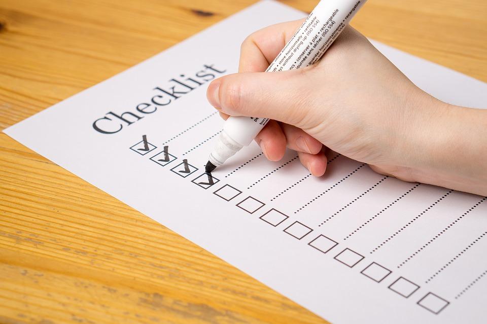 A close up of a hand that is holding a white marker, and ticking off boxes on a checklist. To make a moving checklist is not easy, and it requires a lot of planning.