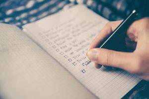 A close up of a person holding a pen and creating a checklist. Learn how to make a moving checklist as soon as possible in order to make the relocation process less difficult. 