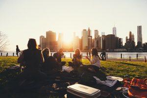 A group of friends on a picnic, which is one of the best outdoor activities in Toronto. We see the city behind them. 