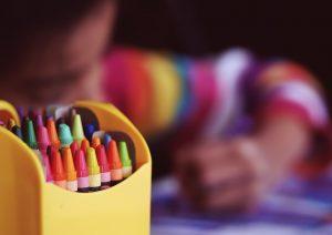 A close up of a box of crayons and a child behind it.