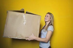 A woman with a box on a yellow background keeping of her moving timeline